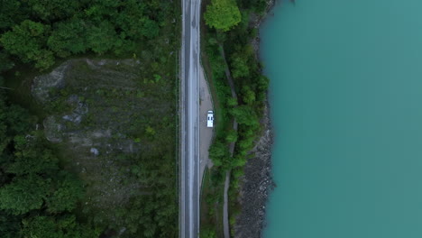 Aerial-view-descending-over-camper-van-parked-on-the-side-of-forest-lake-on-a-road-trip