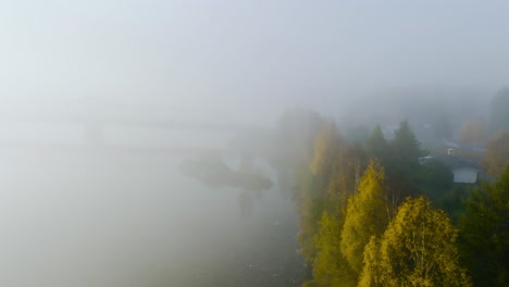 Aerial-view-of-fall-colored-trees-along-a-river,-misty,-autumn-sunrise-in-the-Nordics