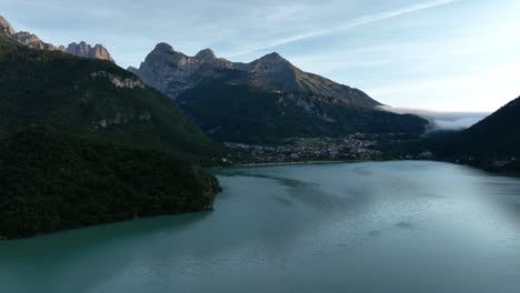 Molveno-lake-aerial-view-towards-town-shore-at-the-base-of-calm-sunrise-valley-slopes