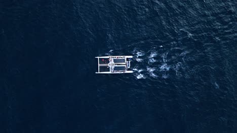 Drone-zenithal-overview-of-catamaran-sailing-in-deep-blue-waters,-isolated-in-ocean