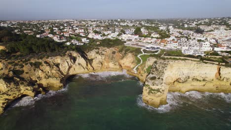 Waves-crash-into-cliffs-and-maritime-town-Carvoeiro-in-Portugal,-aerial