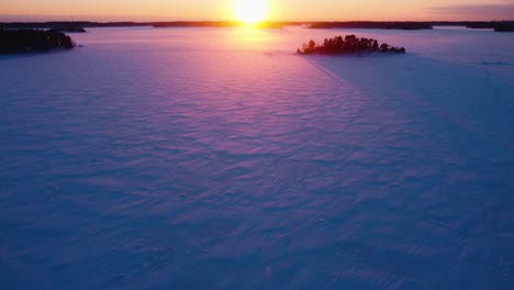 Drone-tilting-over-frozen-sea,-toward-islands-and-the-sunset,-winter-in-Finland