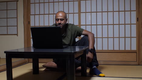 In-Einem-Traditionellen-Japanischen-Interieur-Integriert-Ein-Mann-Moderne-Technologie-Nahtlos-In-Die-Ruhige-Atmosphäre-Und-Arbeitet-An-Seinem-Laptop,-Indem-Er-Den-Deckel-öffnet