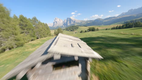 FPV-racing-drone-flying-over-green-valley-with-Dolomites-mountains-in-background