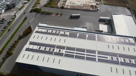 Bird's-eye-aerial-of-solar-panels-installed-on-facility-roof-with-view-over-parking-lot-and-road