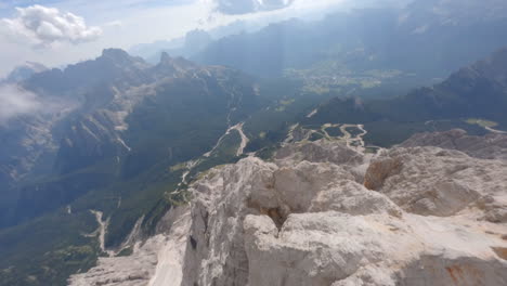 Drone-descending-over-rocky-ridge-of-mountain-peaks-towards-valley-in-summer-season,-Dolomites-in-Italy