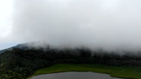 Aerial-hyperlapse-of-white-misty-clouds-rolling-above-Grand-Etang-national-park-volcanic-lake