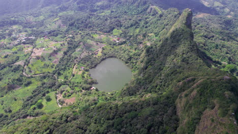 Heart-shaped-lake-nestled-among-lush-green-hills-with-scattered-rural-settlements,-daytime,-aerial-view
