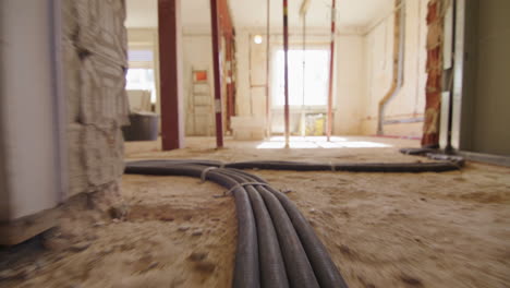 Low-angle-shot-of-following-electric-cables-running-on-the-floor-on-a-construction-site,-entering-a-room-with-huge-windows