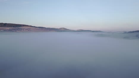 Ruhige-Szenerie-Sanfter-Hügel,-Die-Sich-über-Einer-Riesigen-Nebelfläche-Erheben,-Unter-Einem-Himmel,-Der-Von-Der-Nacht-Zur-Morgendämmerung-übergeht