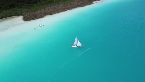 Ein-Segelboot-Auf-Dem-Leuchtend-Blauen-Wasser-Der-Lagune-Von-Bacalar,-Mit-Ruhiger-Umgebung,-Luftaufnahme