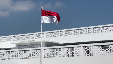 Cámara-Lenta-De-La-Bandera-Roja-Y-Blanca-De-La-Bandera-Indonesia-Ondeando-Frente-Al-Edificio-Blanco-Bajo-El-Cielo-Azul