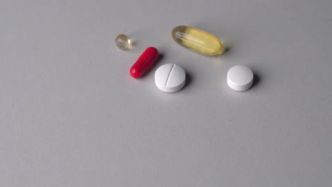 Person-put-multiple-colorful-vitamin-pills-and-capsules-on-table-surface