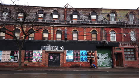 Un-Peatón-Solitario-Camina-Frente-A-Un-Edificio-Abandonado-En-Parkdale,-Toronto
