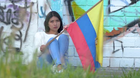 Esperanzada-Y-Triste-Mujer-Latinoamericana-Sosteniendo-La-Bandera-De-Ecuador-Cerca-De-La-Pared-De-Graffiti