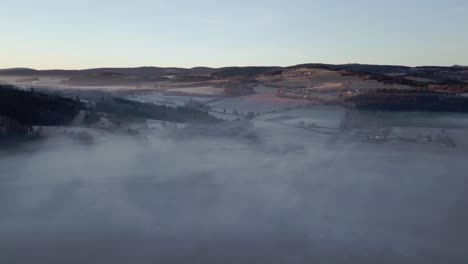 Luftaufnahme-Einer-Ruhigen-Landschaft-Aus-Sanften-Hügeln-Und-Tälern,-Teilweise-In-Nebel-Gehüllt-Im-Sanften-Licht-Der-Morgendämmerung
