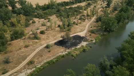 Aerial-view-of-burned-dry-grass-by-the-river-in-sunny-summer,-Europe
