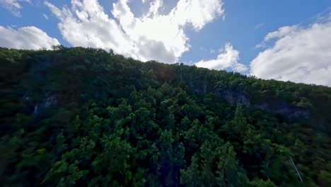 Drone-ascending-over-lush-mountain-and-tropical-forest-with-blue-sky-and-white-clouds-in-background,-Dominican-Republic