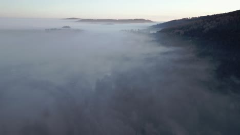 Aerial-view-of-hilly,-serene-landscape-of-a-forested-area-enveloped-in-mist-during-early-morning