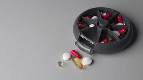 Zoom-in-of-plastic-container-with-pills-and-capsules-inside-on-table-surface
