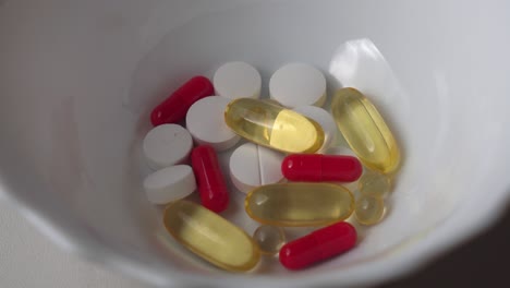 Different-color-vitamin-pills-and-capsules-fall-into-ceramic-container