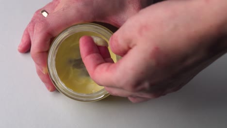 Top-down-view-of-woman-take-homemade-hand-cream-moisturizer-from-glass-jar
