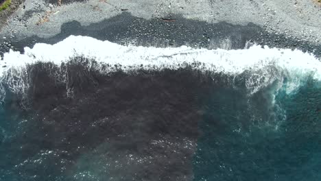 Wide-overhead-aerial-of-ocean-waves-washing-over-stone-beach-in-Hawaii