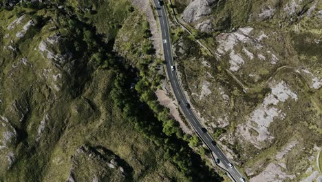Top-down-drop-shot-of-cars-driving-through-Scotland's-rural-and-rocky-countryside