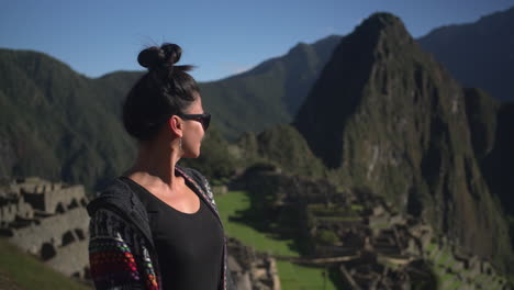 A-female-traveler-gazes-in-admiration-at-the-ruins-of-Machu-Picchu-in-Peru,-with-the-chocolate-shaped-hills-and-animal-shaped-of-the-Andes-Mountains-providing-a-stunning-backdrop