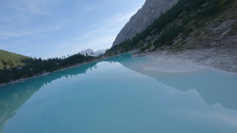 Drone-fpv-flying-over-small-turquoise-glacial-lake-in-summer-season,-Dolomites-mountains,-Italy
