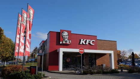 Eingang-Zum-KFC-Fastfood-Restaurant-Mit-Bannern,-Die-Im-Wind-Wehen,-Und-Kunden,-Die-Eintreten