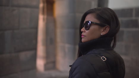 An-Asian-woman,-wearing-sunglasses,-turns-around-to-admire-the-architecture-of-Qorikancha-in-Cusco