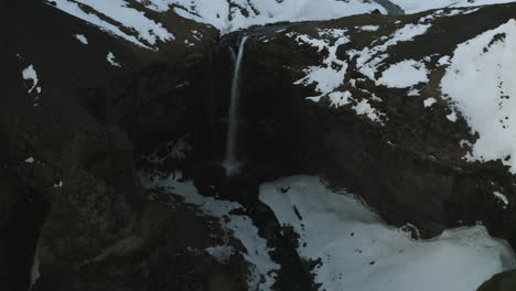 Aerial-reverse-tilt-shot-over-a-waterfall-and-a-gorge,-winter-sunset-in-Iceland
