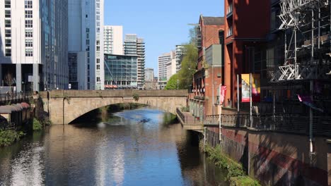 Sonniger-Tagesblick-Auf-Den-Kanal-In-Manchester-Mit-Modernen-Gebäuden-Und-Einer-Alten-Brücke,-Klarer-Blauer-Himmel