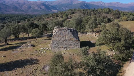 Ascending-flight-with-a-drone-visualizing-a-medieval-tower-in-ruins-on-a-farm-with-stone-walls-next-to-a-dirt-road-with-a-background-of-mountains-in-winter-in-Avila-Spain