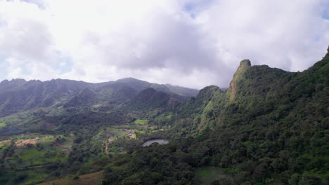 Aerial-view-of-a-lush-green-valley-with-a-mountain-peak-and-lake,-cloudy-sky-above-at-San-Carlos