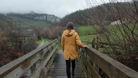Woman-in-Yellow-Coat-Walking-on-Bridge-in-Asturias,-Spain