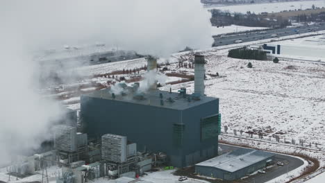 Industrial-plant-with-smokestacks-in-winter,-smoke-billowing-into-sky,-snow-covered-ground,-aerial-view
