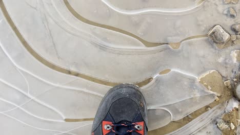 Close-up-POV-shot-of-stepping-onto-a-frozen-puddle-with-walking-boot-and-cracking-the-ice