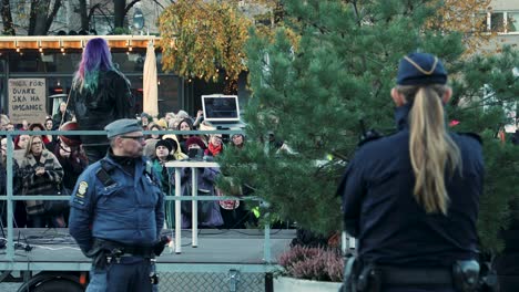 Public-rally-with-a-colorful-haired-speaker-and-attentive-police,-autumn-setting,-daytime,-serious-mood