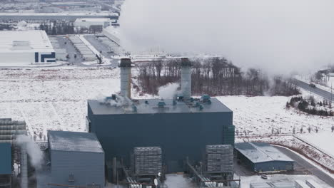 An-industrial-plant-with-multiple-smokestacks,-surrounded-by-snow-covered-ground,-aerial-view