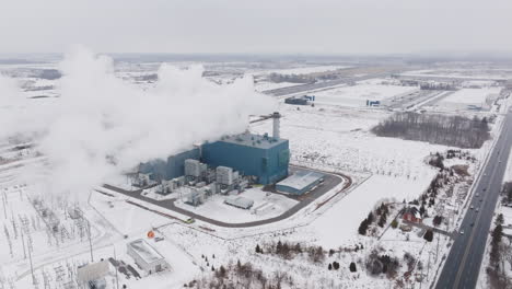 A-large-industrial-plant-emitting-steam-in-a-snowy-landscape,-winter-season,-during-daytime,-aerial-view