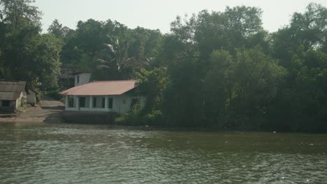 Riverside-house-nestled-among-tropical-trees-with-sunlight-reflecting-off-the-water,-serene-and-secluded