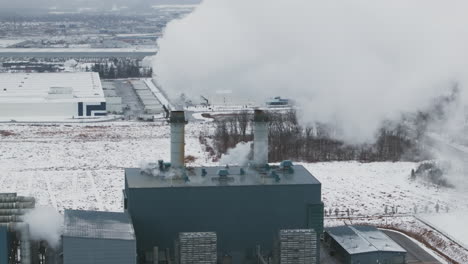 Industrial-facility-emitting-steam-against-a-snowy-landscape,-winter-season,-aerial-view