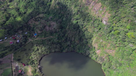 A-secluded-lake-surrounded-by-lush-greenery-and-a-small-community,-aerial-view