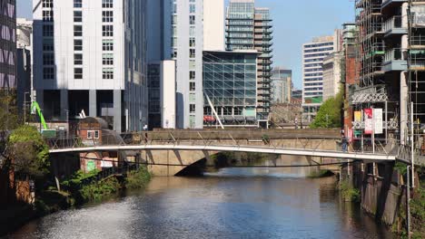 Urban-river-flowing-through-Manchester-with-modern-buildings-and-bridge,-sunny-day