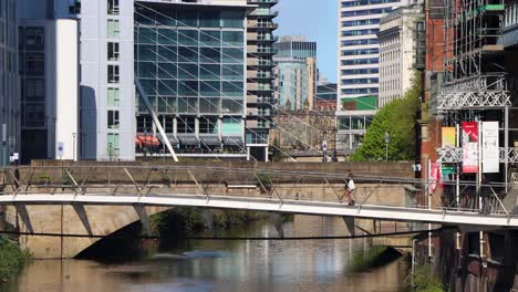 Sunny-day-in-Manchester-with-modern-buildings,-pedestrian-bridge-over-river,-clear-sky