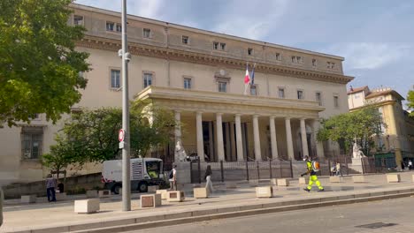 Man-walking-by-a-neoclassical-courthouse-in-Aix-en-Provence,-sunny-day,-street-view