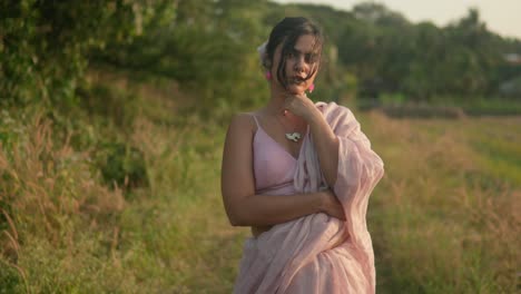 Elegant-woman-in-pink-dress-posing-thoughtfully-in-rural-setting,-golden-hour