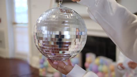 Spinning-shiny-silver-disco-ball-in-hand-and-preparing-room-for-party